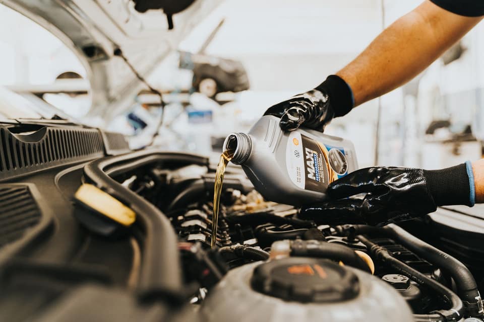 Mecánico echando aceite nuevo en el motor de un coche en un taller