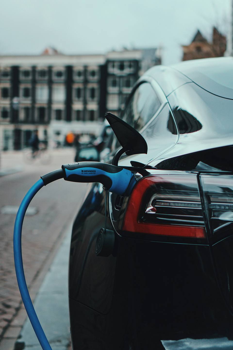 Coche eléctrico negro cargando aparcado en una calle de ciudad, con un cable de carga azul