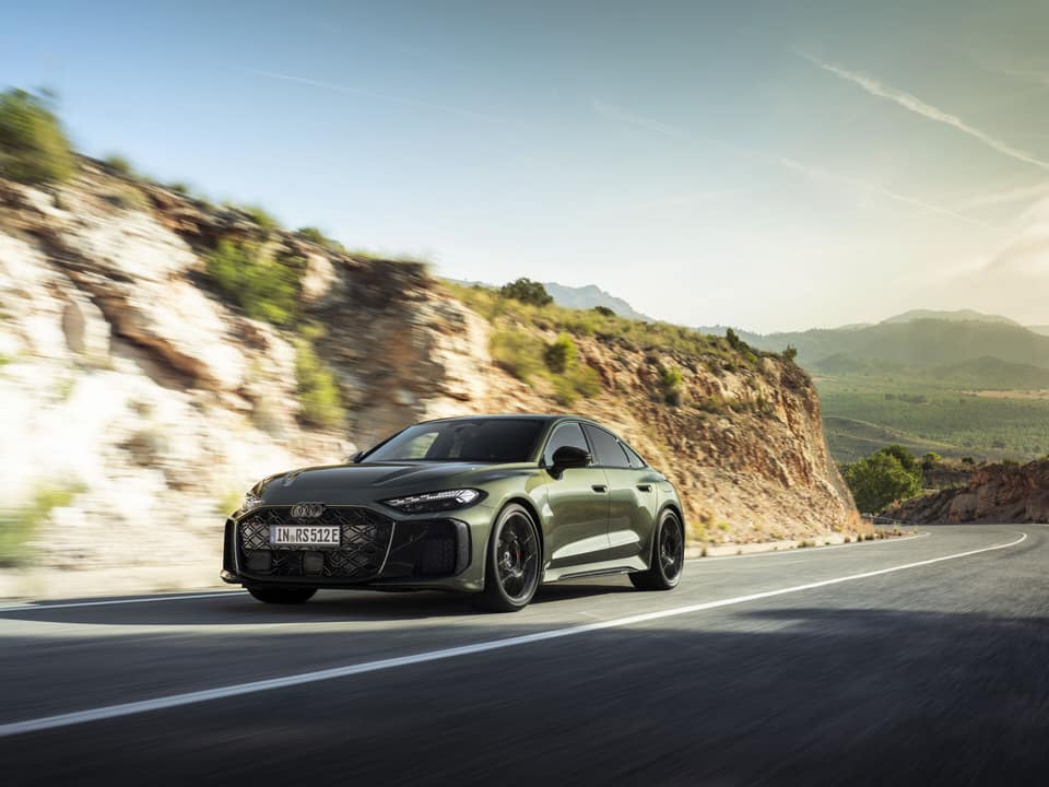 Audi RS 5 berlina híbrido enchufable de 2026 en verde Bedford, vista delantera de tres cuartos en movimiento